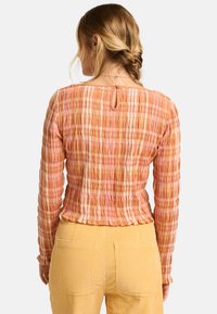 Geweven, oranje en roze gestreepte blouse met lange mouwen en een sleutelgatdetail aan de achterkant. In combinatie met gele ribcord broek.