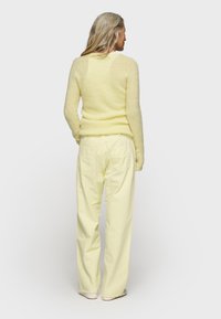 Maglione giallo chiaro, morbido e peloso, con maniche lunghe abbinato a pantaloni giallo chiaro, larghi e a vita alta. Texture morbida, design semplice.