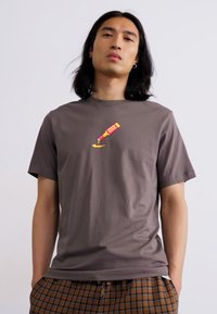 Grå bomulds t-shirt med en grafik af en gul malingtube med pink accenter, præsenteret på en neutral baggrund. Enkel design med rund hals.