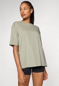 Lys olivengrønn oversized t-skjorte laget av mykt stoff, med korte ermer, rund hals og en liten logo på brystet.