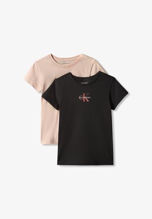 Jong meisje met lang haar dat een lichtroze T-shirt met korte mouwen, losse zwarte broek en zwarte schoenen draagt, staand met handen achter de rug.