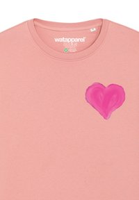 T-shirt en coton rose avec un col rond, présentant un motif de cœur rose texturé, peint à la main, sur le côté gauche de la poitrine.