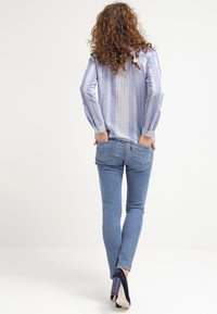 Hellblau gestreiftes langärmliges Hemd, kombiniert mit taillierten hellblauen Jeans, die eine dezente Waschung und ein hinteres Taschendesign aufweisen.