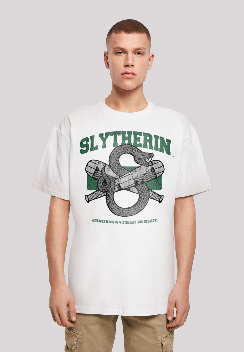 Bílý bavlněný tričko s grafikou Slytherin, která obsahuje design hada a kouzelné hůlky v zelené a šedé barvě. Krátké rukávy, kulatý výstřih. Volný střih.