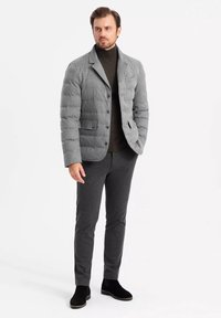 Chaqueta acolchada gris con un acabado texturizado, tres botones y bolsillos con tapa, llevada sobre un suéter de cuello alto oscuro y pantalones grises a juego. Botines negros.