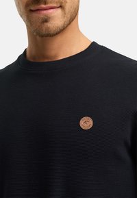 Marine blauwe geribbelde trui met een ronde halslijn, voorzien van een textuurstof en een klein bruin leren logo op de linkerkant.