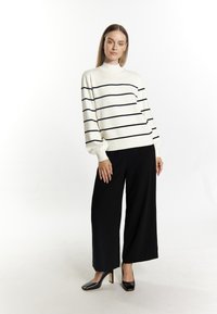 Witte trui met zwarte horizontale strepen, hoge nek en pofmouwen, gecombineerd met zwarte wijde broekspijpen en zwarte hakken.