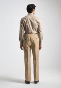 Camisa beige de botones con mangas largas, combinada con pantalones color tostado que tienen bolsillos traseros y un corte recto.