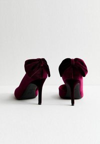 Scarpe con tacco alto in velluto di un profondo bordeaux, con un grande fiocco dietro. Design elegante con punta affusolata e tacco a spillo sottile.