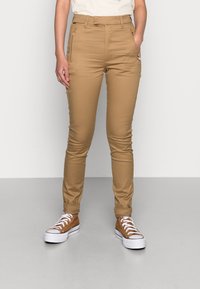 Béžové, vypasované kalhoty s vysokým pasem. Obsahují kapsy na zip a hladký povrch. Ráno s hnědými teniskami a světlou košilí.