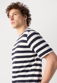 Gestreiftes T-Shirt mit navyblauen und weißen horizontalen Streifen, kurzen Ärmeln, Rundhalsausschnitt, weichem Baumwollmaterial und kleinem, markiertem Logo auf der Brust.