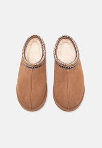 Brune semskede tøfler med en blød, beige inderside, der har en vævet accent langs kraven og en rund tå.