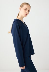 Navyblaues Kapuzensweatshirt aus weichem Material, mit langen Ärmeln, lockerer Passform und V-Ausschnitt. Glatte Textur insgesamt.