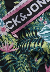 Tissu multicolore avec des motifs de feuilles tropicales et de fleurs, sur fond noir ; comprend une étiquette CK&JONES rose et noire.