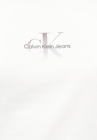 Λογότυπο Calvin Klein Jeans με μεγάλα αλληλοεπικαλυπτόμενα αρχικά "cK" και μικρότερο κείμενο στο κέντρο σε απλό λευκό φόντο.