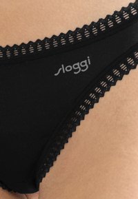 Zwarte onderbroek met kantafwerking en het 'Sloggi' logo, gedragen op de huid.