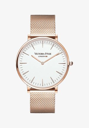 Pyöreä kello, jossa on valkoinen kellotaulu, ruusukultainen verkonauhasti, minimalistiset merkit ja logo "Victoria-Hyde London" kahdentoista kohdalla.