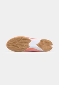 Scarpa sportiva indoor con suola in gomma testurizzata, tomaia bianca e arancione vivace, e motivi a onda distintivi per grip e supporto.