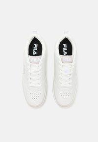 Baskets blanches avec une tige en synthétique lisse, des lacets plats, une boîte à orteils perforée et des semelles intérieures noires arborant le logo FILA en blanc.
