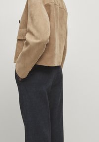 Veste en daim camel au design court, dotée d'une poche latérale et d'une texture lisse, associée à un pantalon bleu marine foncé.