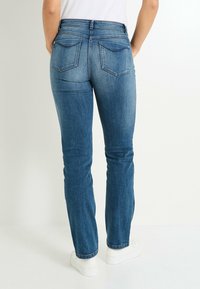 Jean en denim bleu avec une coupe droite, doté de deux poches arrière et d'une taille mi-haute. Le tissu présente un lavage moyen avec un léger délavage.