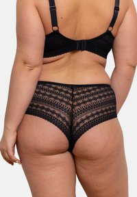 Lingerie en dentelle noire avec des motifs géométriques, des détails transparents et des bords festonnés. Le tissu a une texture douce avec un ajustement extensible.