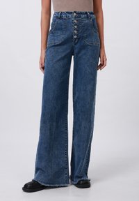 Pantalon en denim bleu à jambes larges avec une taille haute, doté d'une fermeture à cinq boutons, de poches latérales et d'un ourlet effiloché. Texture lisse et tissu résistant.