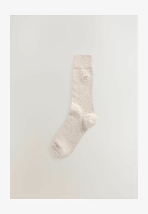 Beige cotton sock with a ribbed cuff, featuring a small embroidered logo near the ankle. Smooth texture, ankle-length design.