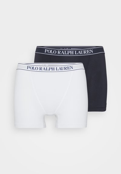 Dve pare bokseric: ene bele in ene mornarsko modre, z teksturirano tkanino in belim pasom z napisom "POLO RALPH LAUREN" v mornarsko modri barvi.