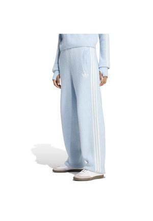 Personne portant un pantalon bleu clair côtelé ample avec des bandes blanches sur les côtés et un logo, associé à des baskets blanches, vu de la taille jusqu'en bas.