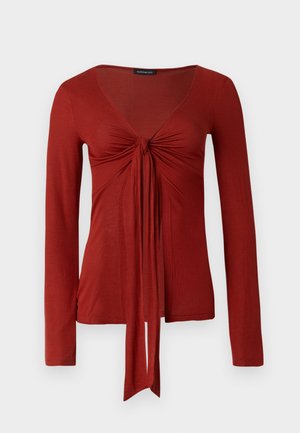 Haut rouge à manches longues avec un col en V profond, un devant froncé et un détail à nouer à la taille ; confectionné dans un tissu doux et extensible.
