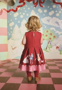 Czerwona sukienka z rozkloszowaną spódnicą, ozdobiona ilustracjami dzieci i zwierząt. Posiada okrągły dekolt i zapięcie na guziki z tyłu.