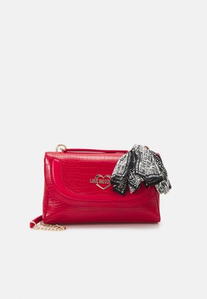 Sac à main rouge à texture crocodile avec logo cœur doré portant l'inscription Love Moschino, décoré d'une écharpe de marque noire et blanche et d'une bandoulière chaîne dorée.