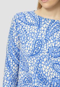 Langarmtop met een blauw-wit abstract patroon, voorzien van een soepele textuur en een ronde halslijn, die ingewikkelde ontwerpelementen laat zien.