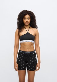 Μαύρο μπραλέτο με λευκή λωρίδα λογότυπου Calvin Klein και μαύρο floral μοτίβο στα σορτς, με λεία υφή και εφαρμοστή σχεδίαση.