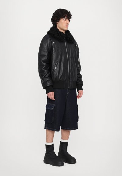 Zwarte leren bomberjack met een fluffy zwarte kraag, gecombineerd met donkere denim cargo shorts en zwarte enkellaarsjes.