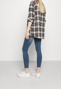 Camisa de franela a cuadros, en blanco y negro, diseño oversized. Jeans ajustados de mezclilla azul con cremalleras en los tobillos. Zapatillas blancas con suelas texturizadas.