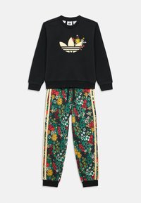 Μαύρο φούτερ με χρυσό λογότυπο στολισμένο με λουλούδια. Πράσινο παντελόνι φόρμας με λουλουδάτο μοτίβο σε κίτρινο και κόκκινο, με πλαϊνές ρίγες και ριμπ μανσέτες.