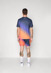 Kurzärmliges Sporthemd mit Farbverlauf und Shorts in tiefblauen bis orangefarbenen Tönen, mit einem glatten Stoff und einem Logodetail auf der Rückseite.