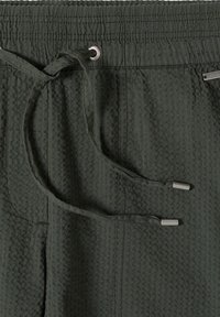 Pantalon en tissu texturé vert foncé avec une taille élastique et des cordons assortis munis d'embouts métalliques.