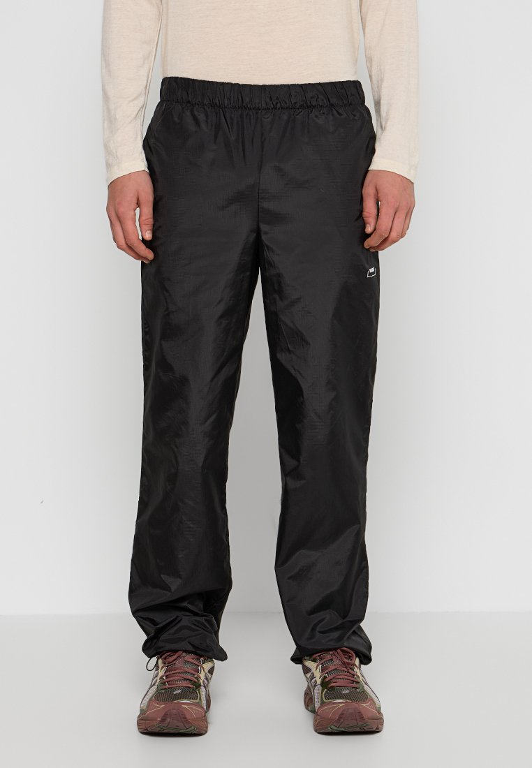 Zwarte sportbroek met een elastische tailleband, lichtgewicht materiaal, een subtiele glans en een klein logo op de linkeronderbeen.
