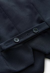 Marineblauw, gestructureerd stof met verticale strepen, voorzien van twee zwarte knopen en een op maat gemaakte zoom.