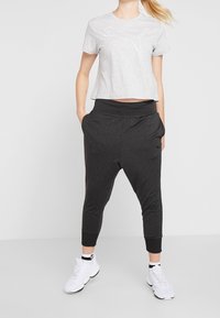 Grå kortärmad t-shirt med vitt Puma-logga, matchad med svarta joggerbyxor med sidofickor och smalnande fållar. Vita träningsskor.