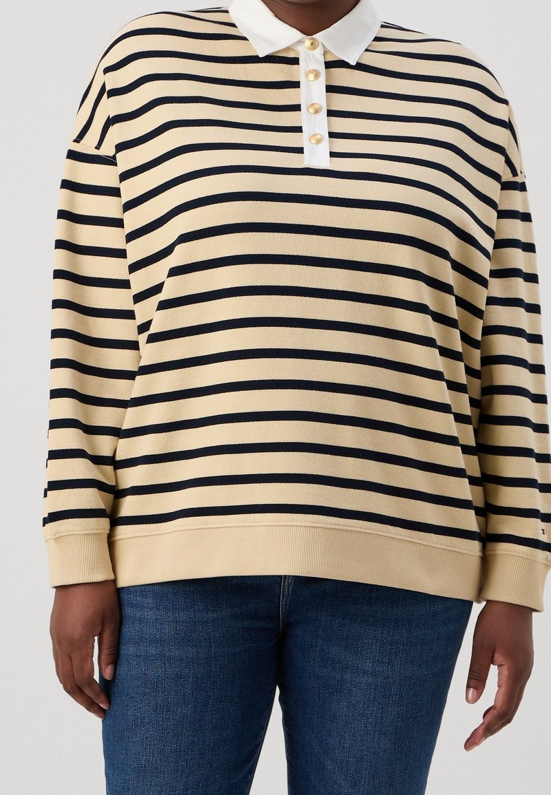 Jersey a rayas en beige con rayas marinas, con cuello blanco y botones dorados. Corte relajado con puños y dobladillo de canalé.