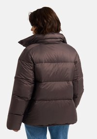 Veste matelassée marron avec un col montant, design matelassé et texture lisse et brillante, associée à un jean bleu clair.