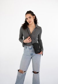 Black crossbody bag with a smooth texture. Worn with a gray long-sleeve shirt and light blue distressed wide-leg jeans.