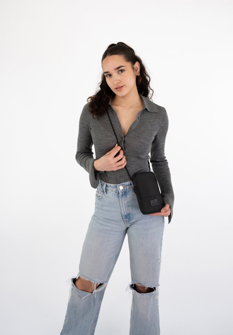 Black crossbody bag with a smooth texture. Worn with a gray long-sleeve shirt and light blue distressed wide-leg jeans.