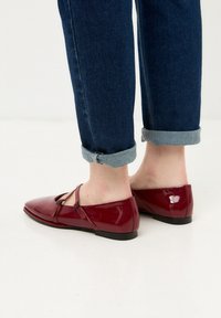 Rote Lackleder-Ballerinas mit spitzer Zehenform, Ausschnittdetails und flachem Absatz. Getragen mit hochgekrempelten dunklen Jeans.