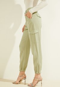 Vaaleanvihreät cargo-housut, joissa on joustavat hihnat, sivutaskut ja korkea vyötärö. Yhdistettyinä nauhoilla varustettuihin, kuviollisiin korkokenkiin.