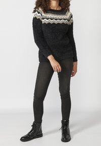 Schwarzer, flauschiger Pullover mit einem Zickzackmuster in Gold-, Silber- und Grautönen, kombiniert mit schwarzen Skinny Jeans und schwarzen Schnürstiefeletten.